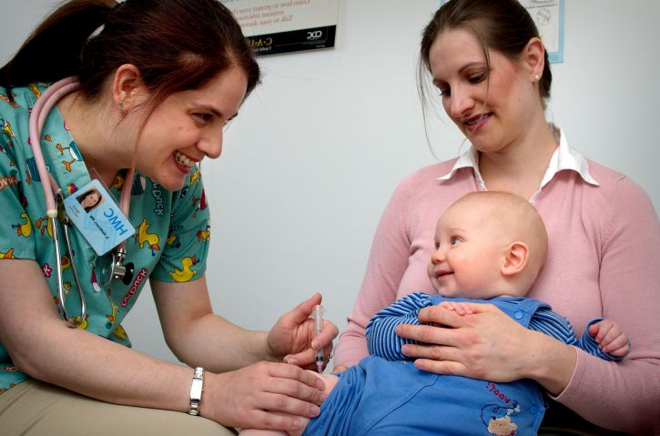 Nurse vaccinates smiling baby.